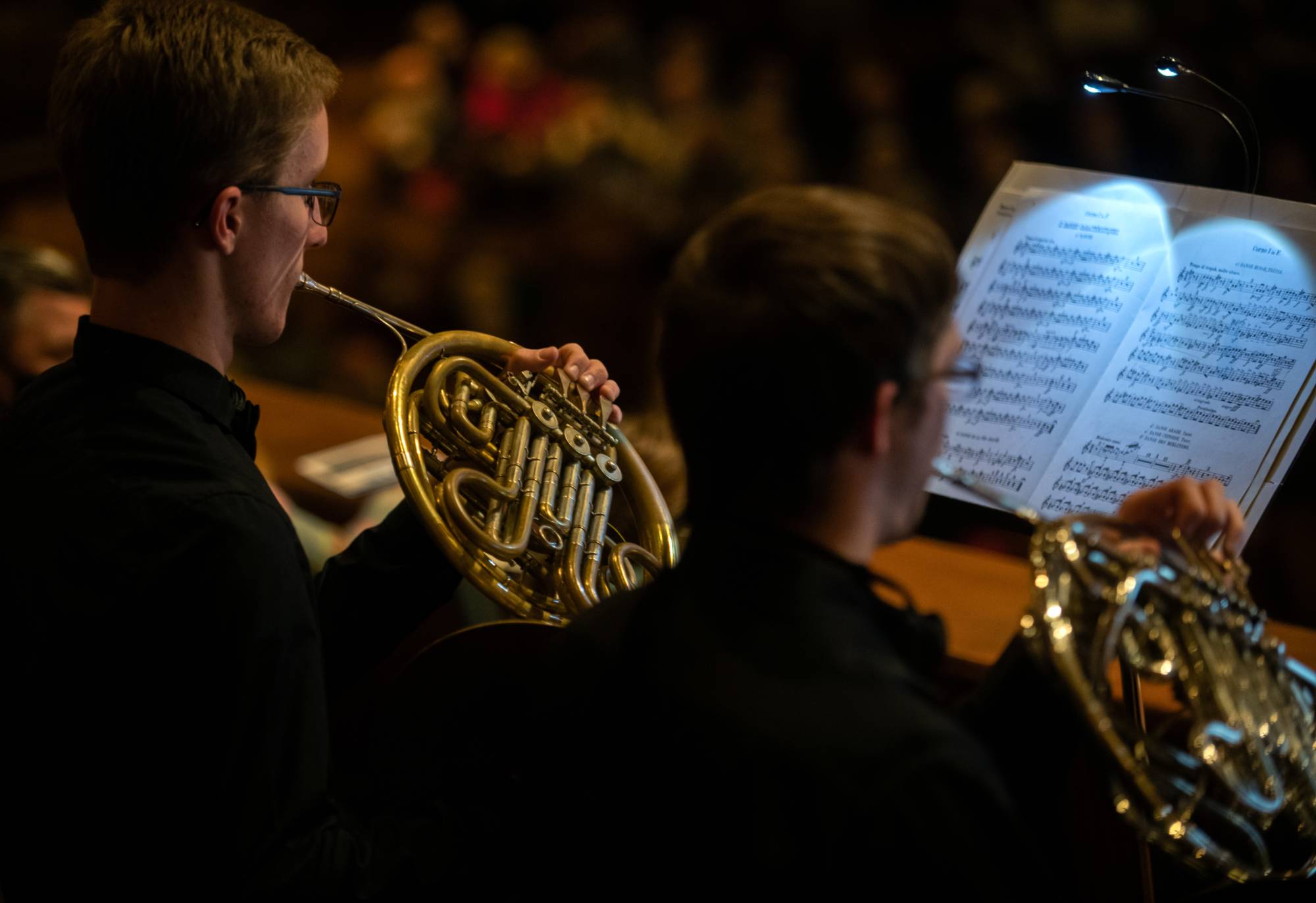 Pictured from behind, two students play their brass instruments
